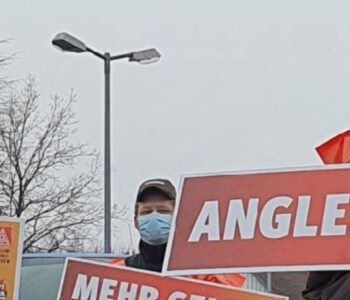 Streikende mit Atemschutzmasken und Schildern mit Forderungen; Sicherheit, Zukunft, Angleichung.