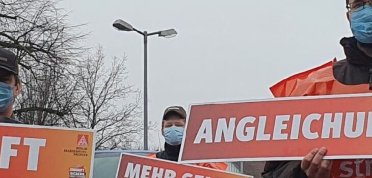 Streikende mit Atemschutzmasken und Schildern mit Forderungen; Sicherheit, Zukunft, Angleichung.