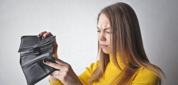 Eine Frau wirft einen frustrierten Blick in einen leeren Geldbeutel