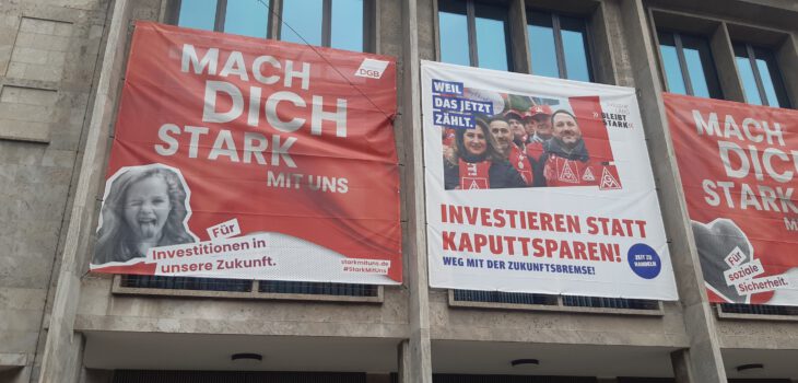 Transparente an einer Hauswand mit Aufrufen zur Mitarbeit und für Investitionten statt Sparwahn